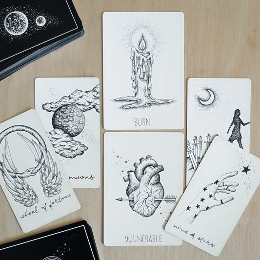 Tarot cards from The Wandering moon tarot and oracle cards from The Wandering soul oracle deck, being used together. Both indie decks, by MoonHaus Studio, are in black and white, with fine detail black line work with stippling. 