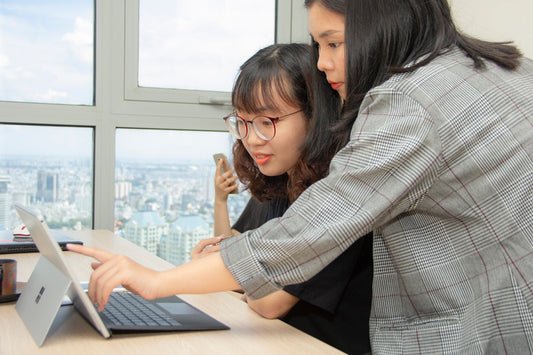woman standing behind sitting woman in front of laptop computer