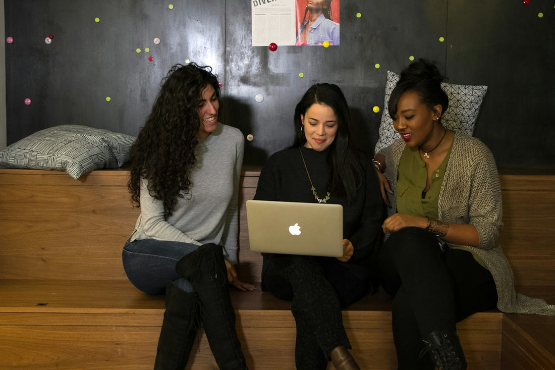 three women sitting on a bed looking at a laptop