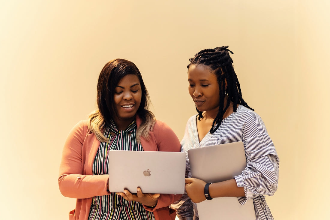 A couple of women standing next to each other with laptops