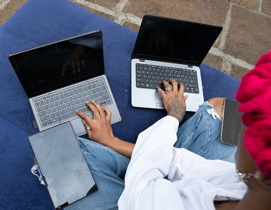 Two people using laptops outdoors on a blue cushion.